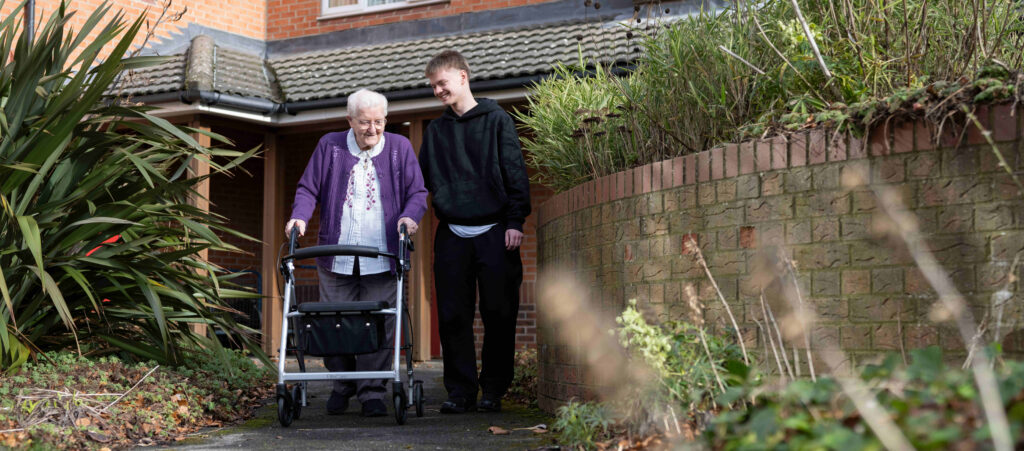 Woman walking through a garden using a rollator, accompanied by a man. They are both laughing.